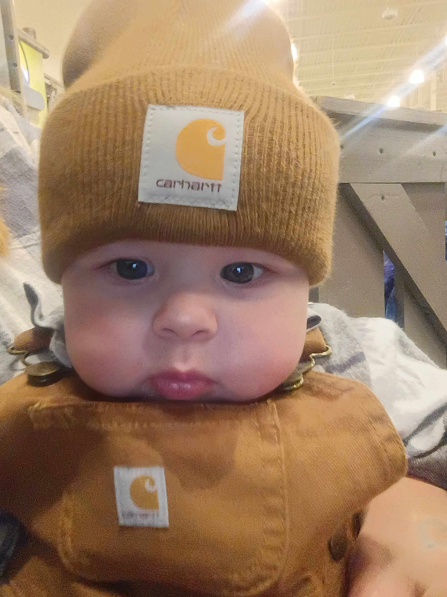 Easton joined the competition — help win amazing prizes! baby, infant, child, beanie, knit_hat, carhartt_label, overalls, bib, chubby_cheeks, eyes, lips, close_up, portrait, indoor, store, wooden_railing, soft_lighting, brown_clothing, adorable, casual_clothing