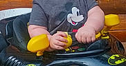Easton joined the competition — help win amazing prizes! baby, batman_logo, black, chubby_cheeks, closeup, face, gray_tshirt, hands, head, indoors, infant, laughing, mickey_mouse, playful, seat, smiling, toy_car, walker_toy, wooden_background, yellow