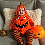 Alma a rejoint le concours — aidez-le/la à gagner de superbes lots ! baby, pumpkin_costume, orange, black_stripes, couch, pillow, halloween, smile, child, indoor, toy_pumpkin, costume, striped_tights, cute, happy, face, person, decor, festive, cozy