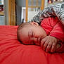baby, sleeping, bed, blanket, red_bedspread, hand, face, infant, indoors, cozy, peaceful, child, soft_lighting, patterned_blanket, portrait, resting, cute, closeup, young_child, toddler