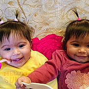 Lyanna And Leslie is registered to the contest to win money with this photo: baby, twins, infant, smile, pigtails, hair_ties, blanket, pink_toy, yellow_shirt, mauve_shirt, cheeks, eyes, face, indoor, portrait, happy, sibling, cute, bowl, playtime
