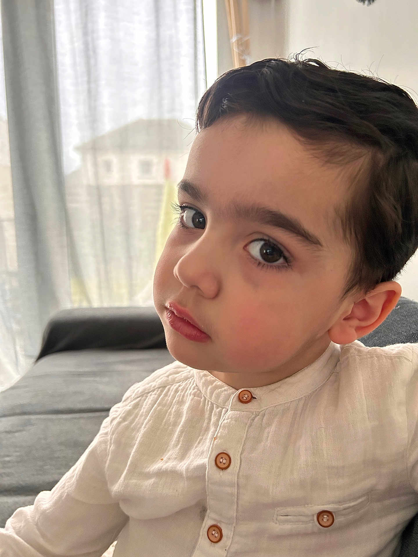 Malhon participe au concours pour gagner de l'argent avec cette photo : child, portrait, indoor, couch, white_shirt, buttoned_shirt, curtains, natural_light, face, young_boy, expression, seated, casual_clothing, home, soft_light, brown_hair, closeup, looking, person, skin