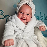 Frankie joined the competition — help win amazing prizes! baby, background, bathrobe, child, chubby_cheeks, cute, expression, face, happy, headwear, indoors, infant, person, portrait, seated, skin, smiling, soft_texture, towel, white