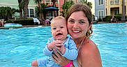 Colson joined the competition — help win amazing prizes! woman, baby, swimming_pool, water, smile, happy, outdoor, sunny, resort, vacation, family, child, holding, building, palm_tree, summer, people, blue_sky, playful, relaxation