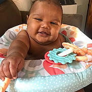 Daniel is registered to the contest to win money with this photo: baby, child, infant, smiling, happy, teething_toy, colorful, polka_dot, baby_seat, arm, hand, face, cheeks, indoors, furniture, couch, living_room, skin, cute, playful
