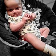 Coco is registered to the contest to win money with this photo: baby, infant, child, onesie, floral_pattern, socks, baby_chair, cartoon, paw_print, smile, hands, face, cute, indoor, wood_floor, seat, comfort, playful, portrait, soft_lighting