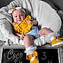 Coco is registered to the contest to win money with this photo: baby, infant, smiling, headband, yellow_bib, blue_onesie, white_chair, fluffy_cushion, pearl_necklace, yellow_shoes, chalkboard, milestone, portrait, cute, cozy, indoor, child, happy, sitting, decor