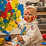 toddler, child, paint, paintbrush, face_paint, smock, colorful, art, studio, floor, messy, expression, sitting, blue, yellow, red, creative, portrait, indoor, playful
