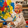 toddler, child, paint, paintbrush, canvas, art, messy, face_paint, floor, studio, creative, colorful, white_smock, smiling, blue_paint, yellow_paint, red_paint, barefoot, indoor, playful