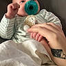 Fallon is registered to the contest to win money with this photo: baby, pacifier, striped_clothing, hand_holding, plush_toy, blanket, infant, sleepwear, tattoo, couch, comfort, indoor, person, newborn, closeup, skin, bedroom, rest, cozy, care