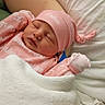 Fallon is registered to the contest to win money with this photo: newborn, baby, sleeping, pink_clothing, hat, blanket, bed, human_arm, infant, cozy, resting, cute, soft, wrapped, child, person, portrait, indoor, peaceful, newborn_baby