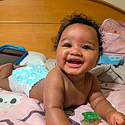 Zalyn joined the competition — help win amazing prizes! baby, infant, child, smiling, laughing, portrait, indoor, bedroom, bed, bedding, wooden_headboard, curly_hair, diaper, pacifier, tablet, pillow, blanket, sitting, lying_down, happy