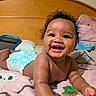 baby, infant, child, smiling, laughing, portrait, indoor, bedroom, bed, bedding, wooden_headboard, curly_hair, diaper, pacifier, tablet, pillow, blanket, sitting, lying_down, happy