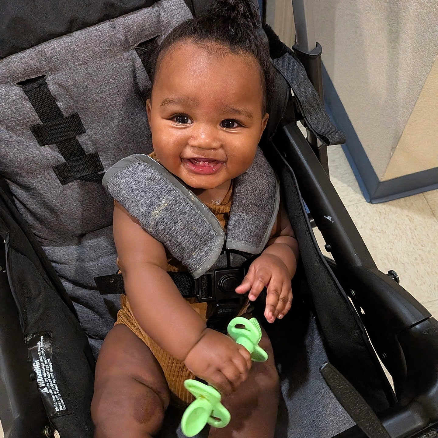 Zalyn joined the competition — help win amazing prizes! baby, child, infant, stroller, smiling, happy, portrait, indoor, toy, green_toy, seated, baby_carriage, harness, clothing, brown_outfit, curly_hair, face, hands, legs, floor