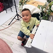 Michael joined the competition — help win amazing prizes! child, toddler, piano, keyboard, studio, flowers, wooden_table, stool, tripod, cord, sneakers, denim_shorts, sweatshirt, smile, portrait, indoor, white_floor, decor, hands, curious