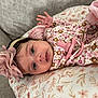 Sadie is registered to the contest to win money with this photo: baby, infant, flower_headband, pacifier, pink, cushion, floral_pattern, clothing, hand, face, eyes, cute, lying_down, comfort, indoors, child, newborn, soft, head, person