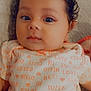 baby, infant, curly_hair, onesie, text_print, face, portrait, close_up, cute, child, indoors, soft_lighting, looking_at_camera, expression, skin, head, person, newborn, lying_down, cozy