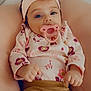 Sadie joined the competition — help win amazing prizes! baby, infant, pacifier, headband, flower, blue_eyes, cushion, clothing, floral_pattern, pants, portrait, cute, child, indoors, soft_texture, relaxed, lying_down, skin, hand, small_fingers