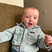 Luca is registered to the contest to win money with this photo: baby, buttoned_shirt, casual_clothing, child, comfortable, couch, cute, denim_shirt, face, happy, home, indoor, jeans, person, portrait, seated, short_hair, smiling, toddler, young_child