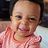 adorable, baby, bed, candid, child, close_up, coral_outfit, cozy, curly_hair, face, happy, head, indoors, infant, portrait, sitting, smiling, soft_lighting, striped_clothing, tongue_out