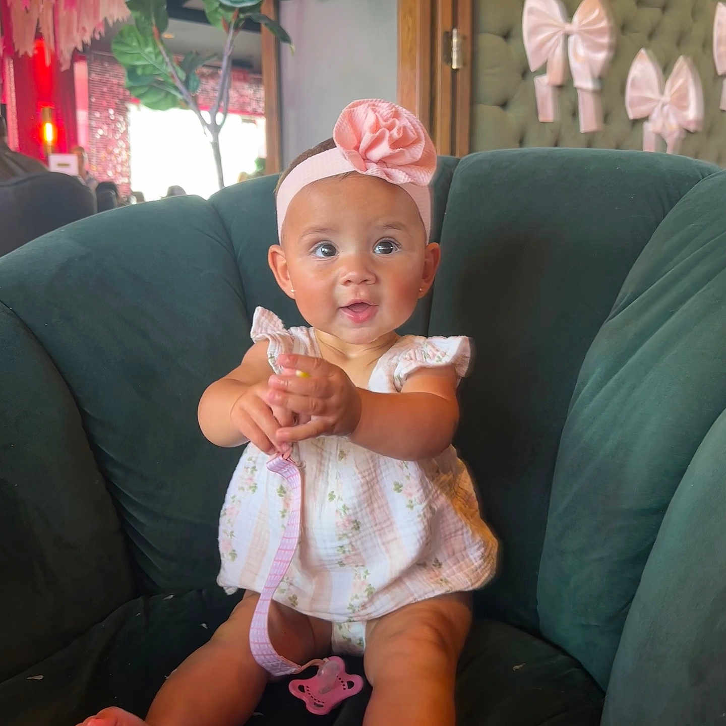 Emerson is registered to the contest to win money with this photo: baby, child, clothing, cute, decor, dress, flower, green_chair, happy, headband, indoor, infant, pacifier, person, pink, portrait, sitting, smiling, toes, wall_bows