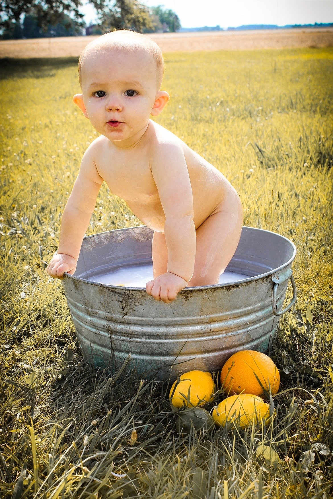 Elijah joined the competition — help win amazing prizes! baby, child, metal_tub, water, outdoor, grass, sunlight, field, fruit, orange, lemon, citrus, nature, bare_skin, summer, playful, curious, young, standing, bath