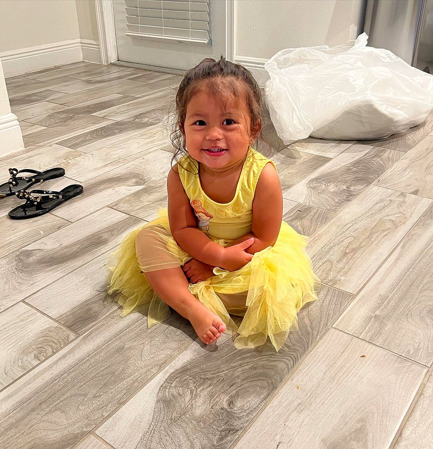 Jolie is registered to the contest to win money with this photo: baby, baby_toddler_clothing, cheek, child, comfort, crawling, door, floor, flooring, fun, grass, happy, hardwood, human_leg, joy, person, sitting, skin, smile, toddler