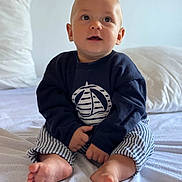 Louis participe au concours pour gagner de l'argent avec cette photo : baby, child, infant, sitting, bed, blue_clothing, striped_pants, barefoot, indoors, soft_light, cute, portrait, curious, face, hands, feet, pillow, blanket, home, casual
