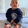 baby, child, infant, sitting, bed, blue_clothing, striped_pants, barefoot, indoors, soft_light, cute, portrait, curious, face, hands, feet, pillow, blanket, home, casual