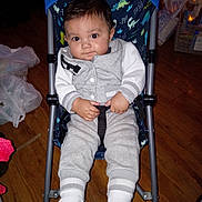 Matteo joined the competition — help win amazing prizes! baby, child, stroller, indoor, floor, wooden_floor, clothing, socks, seatbelt, person, infant, grey_outfit, dinosaur_pattern, hands, face, eyes, expression, footwear, baby_stroller, casual