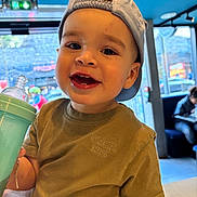 Kaïs a rejoint le concours — aidez-le/la à gagner de superbes lots ! toddler, child, smiling, cap, indoor, cafe, sippy_cup, clothing, face, person, table, window, daylight, happy, casual, young_child, seated, background_people, light, portrait