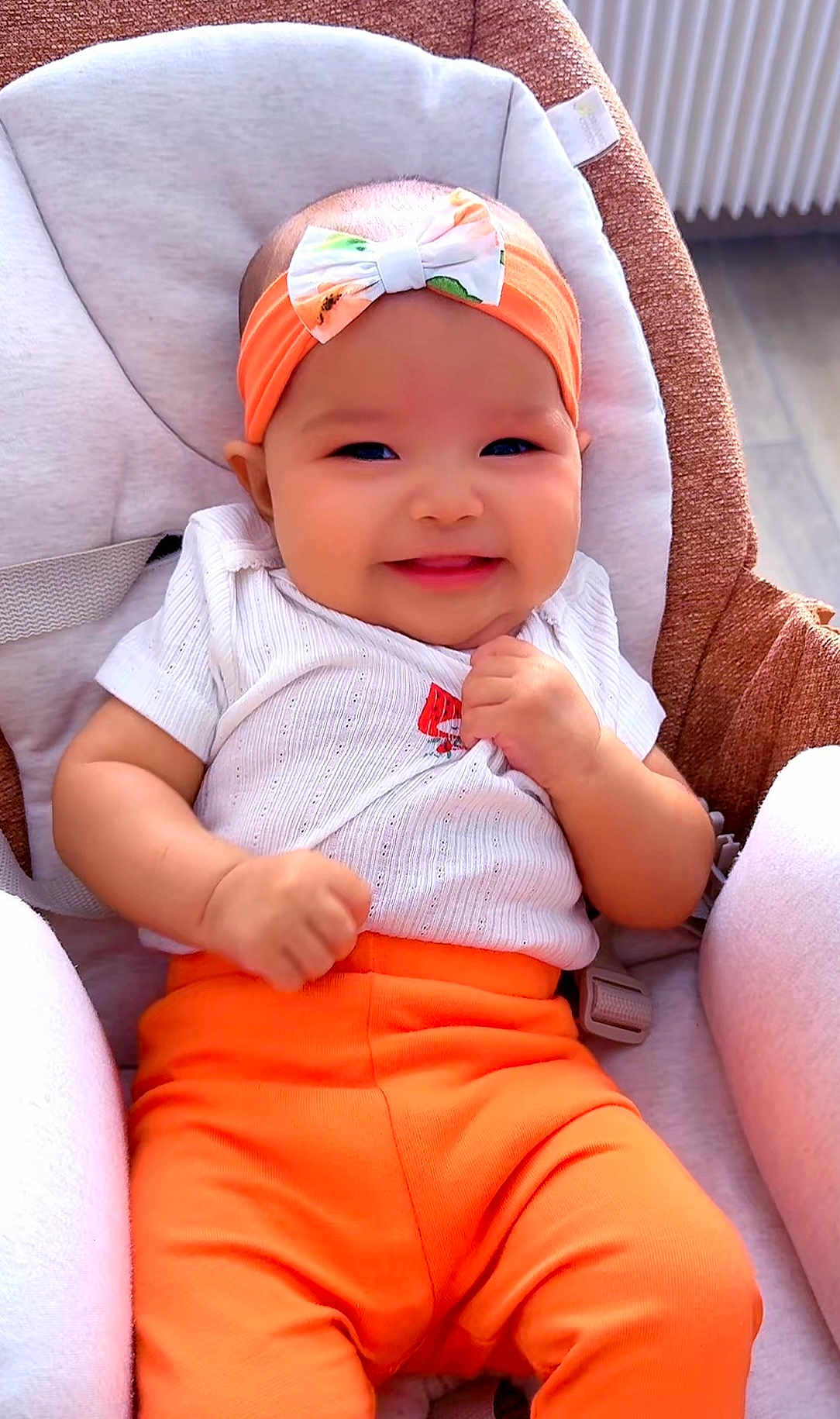 Mikanto participe au concours pour gagner de l'argent avec cette photo : baby, infant, smile, headband, bow, orange_pants, white_shirt, baby_seat, cushion, happy, cute, child, indoors, portrait, person, clothing, seatbelt, skin, hands, face