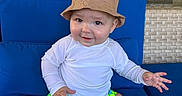 Andre joined the competition — help win amazing prizes! baby, child, smiling, hat, bucket_hat, white_shirt, green_shorts, floral_pattern, blue_cushion, sitting, indoor, window, reflection, sunlight, playful, happy, person, foot, hand, casual_clothing