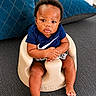 Messiah is registered to the contest to win money with this photo: baby, infant, child, seat, couch, blue_pillow, home_interior, plant, decor, clothing, navy_shirt, sitting, barefoot, hands, face, expression, indoors, furniture, soft_toys, comfort