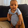 baby, infant, onesie, smiling, hands, couch, curtains, indoors, person, child, happy, tongue_out, holding, skin, face, arm, leg, seated, casual, home