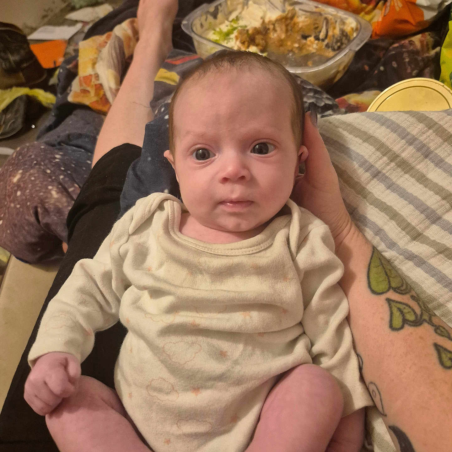 Brooklynn joined the competition — help win amazing prizes! baby, infant, person, clothing, hand, leg, tattoo, blanket, food_container, snack_bag, couch, room, indoor, casual, sitting, wide_eyes, curious, skin, foot, relaxed