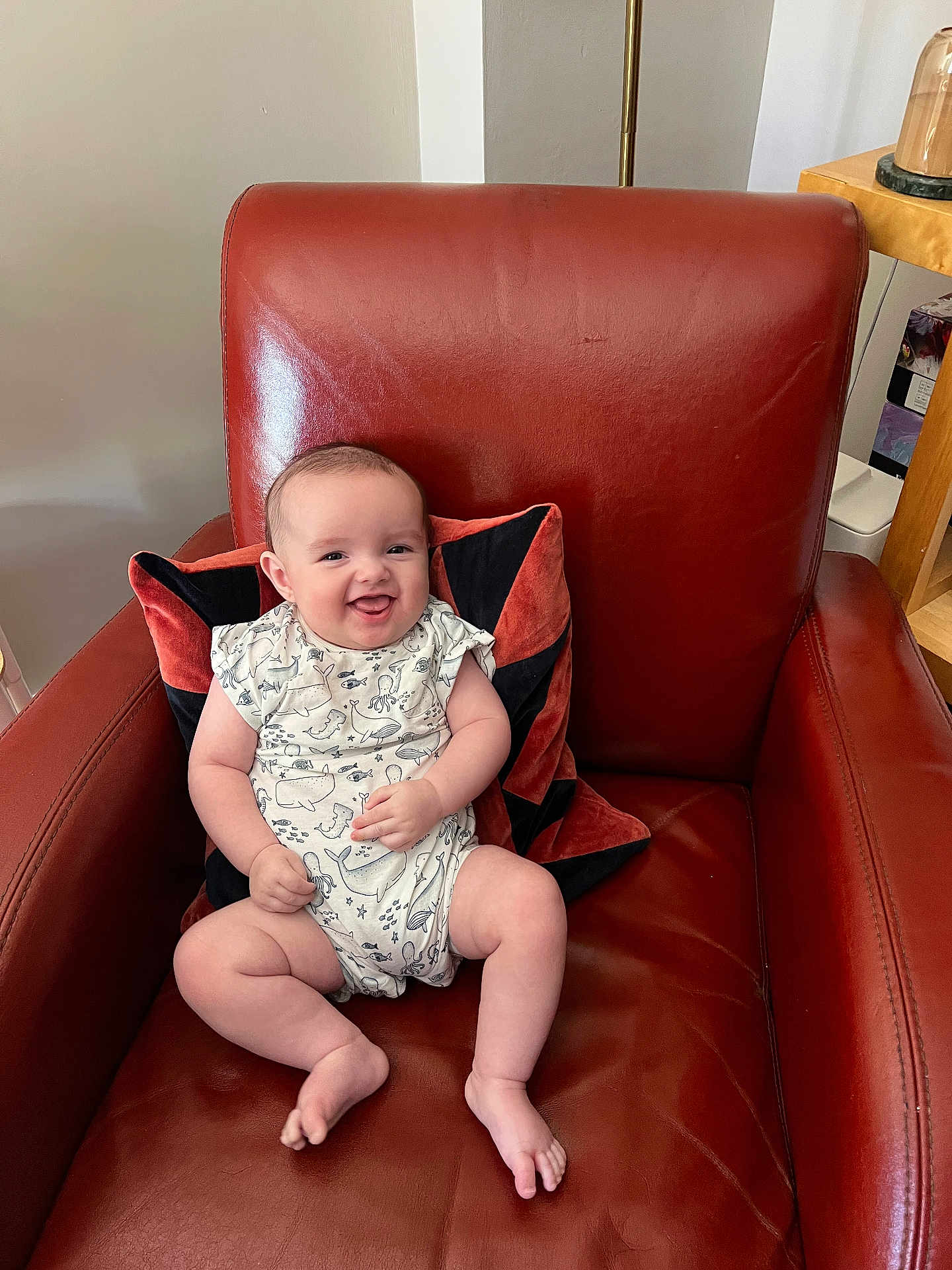 Henry joined the competition — help win amazing prizes! baby, child, smiling, armchair, red_leather, cushion, indoor, happy, infant, person, sitting, cute, comfortable, clothing, patterned, face, legs, feet, home, furniture