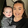 Henry is registered to the contest to win money with this photo: baby, black_shirt, casual_clothing, child, clock, closeup, face, family, grey_clothing, happy, holding, home, indoor, jewelry, long_hair, person, portrait, smile, stairs, woman