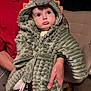 adult_hand, baby, child, closeup, costume, couch, cute, dinosaur_costume, expression, furniture, holding, hood, indoor, person, plush, portrait, pout, red_shirt, soft_texture, tattoo