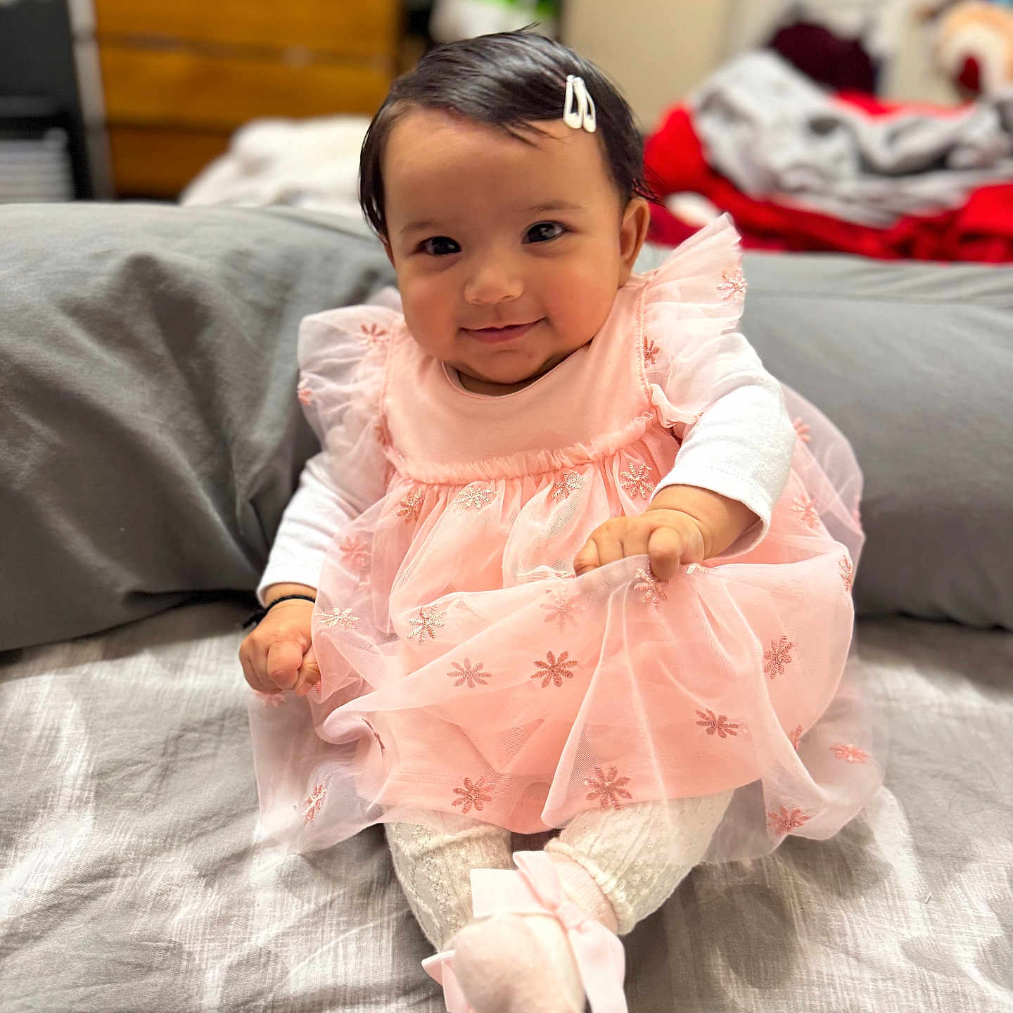 Harleen joined the competition — help win amazing prizes! baby, bed, blanket, child, clothing, cozy, cute, fabric, girl, hair_clip, happy, indoor, infant, person, pink_dress, portrait, sitting, smile, socks, soft_lighting