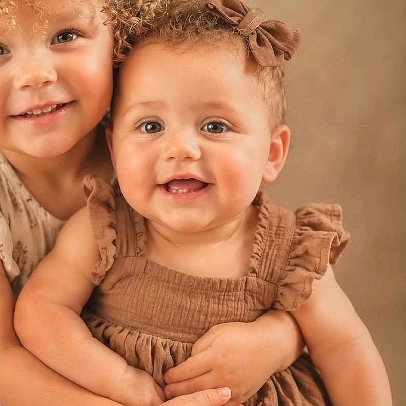 Nevaeh is registered to the contest to win money with this photo: child, children, baby, toddler, curly_hair, brown_dress, smiling, hugging, portrait, cute, happy, sibling, family, studio, warm_tones, indoor, skin, face, head, eyes