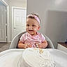 Nevaeh is registered to the contest to win money with this photo: toddler, child, cake, frosting, high_chair, pink_headband, pink_shirt, smiling, messy_face, happy, indoor, celebration, food, birthday, curly_hair, plate, table, person, cute, fun