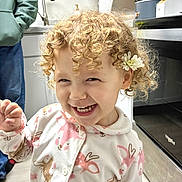 Iris joined the competition — help win amazing prizes! toddler, child, curly_hair, flower, pajamas, smiling, indoor, kitchen, person, appliance, hoodie, cabinet, floor, oven, sink, hand, cute, happy, portrait, home