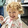 toddler, child, curly_hair, flower, pajamas, smiling, indoor, kitchen, person, appliance, hoodie, cabinet, floor, oven, sink, hand, cute, happy, portrait, home