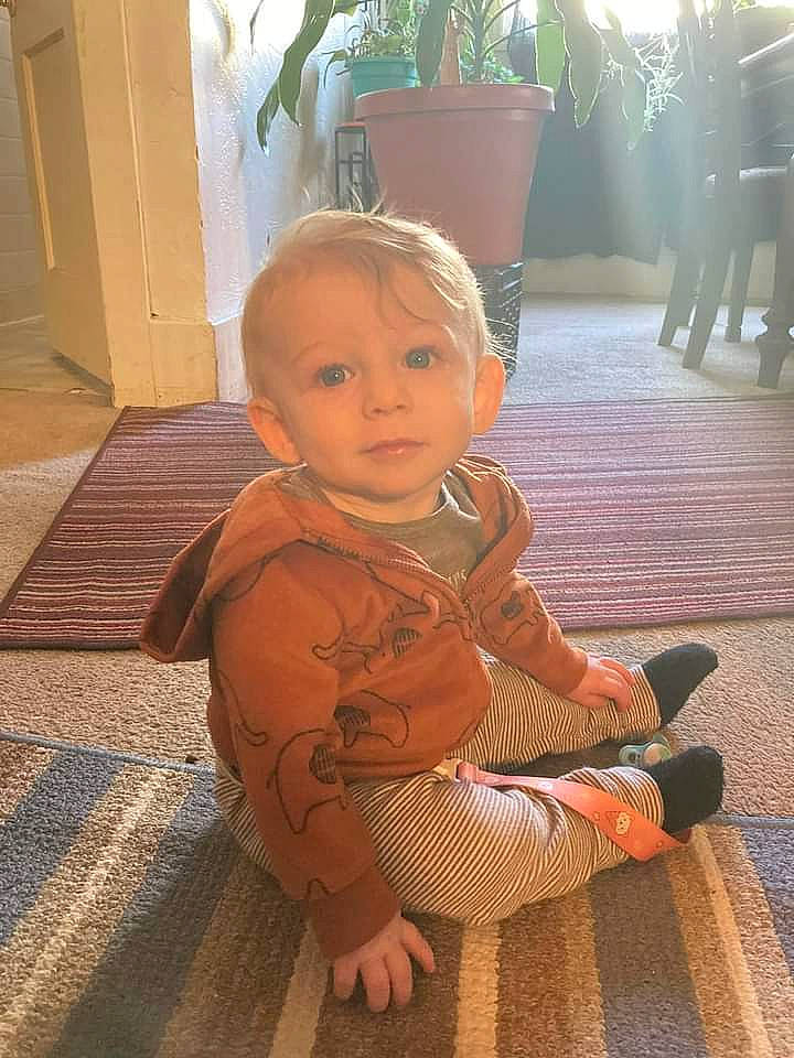 Colton is registered to the contest to win money with this photo: baby, baby_toddler_clothing, carpet, chair, cheek, child, floor, flooring, flowerpot, foot, fun, grass, hardwood, houseplant, human_leg, person, plant, room, sitting, toddler