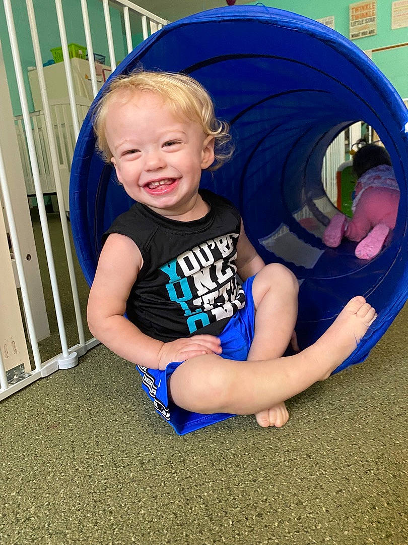 Braxley is registered to the contest to win money with this photo: automotive_tire, azure, baby_toddler_clothing, blue, electric_blue, eye, flooring, fun, grass, hairstyle, happy, human_leg, joy, leisure, person, recreation, sitting, sleeve, smile, t_shirt