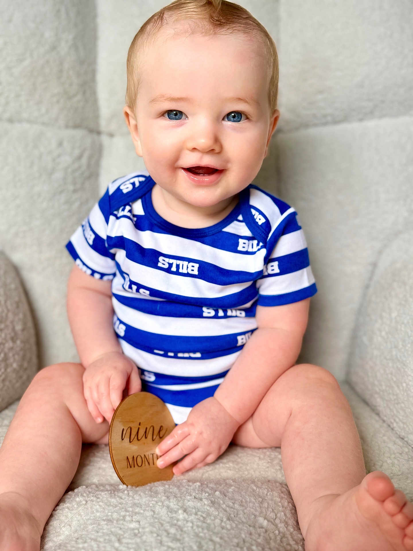 Benson is registered to the contest to win money with this photo: baby, child, blue_eyes, smiling, onesie, striped_clothing, sitting, plaque, wooden_plaque, milestone, indoor, soft_texture, cozy, happy, portrait, cute, chubby_arms, chubby_legs, face, hands