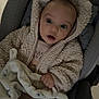 baby, child, infant, car_seat, blanket, plush_toy, clothing, hooded_jacket, hand, face, wide_eyes, indoor, floor, tile_floor, comfort, warm_clothing, expression, seated, cute, portrait