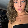 woman, human_face, cat, black_cat, portrait, selfie, curly_hair, blue_eyes, necklace, hoop_earrings, makeup, strapless_top, shoulder, pet, indoor, bedroom, bed, fur, closeup, flash_lighting