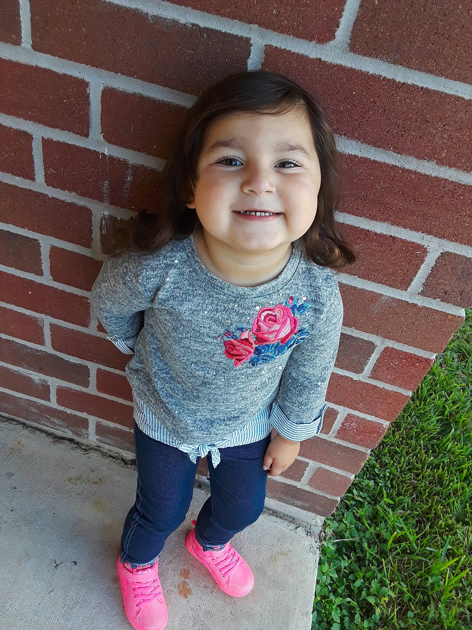 Leah is registered to the contest to win money with this photo: cheek, child, face, footwear, grass, happy, head, jeans, joy, outerwear, pattern, person, pink, shoe, skin, smile, standing, t_shirt, textile, toddler